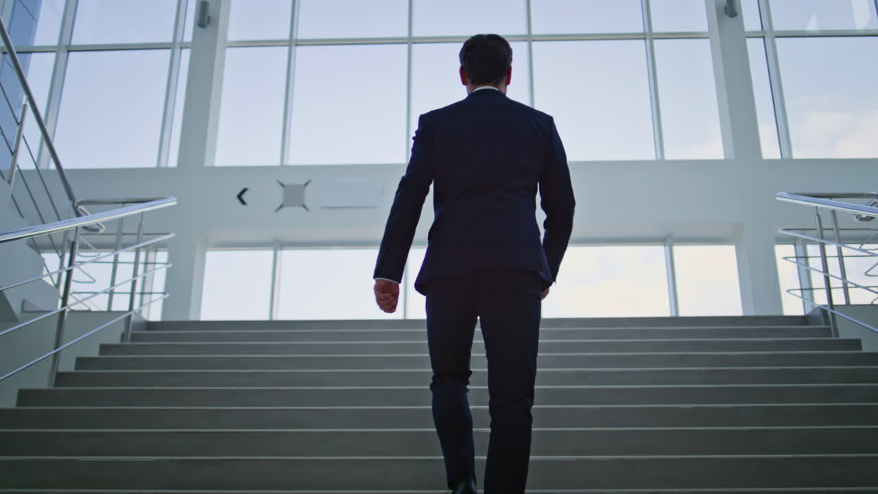 Determined businessman walking upstairs in light modern office back view