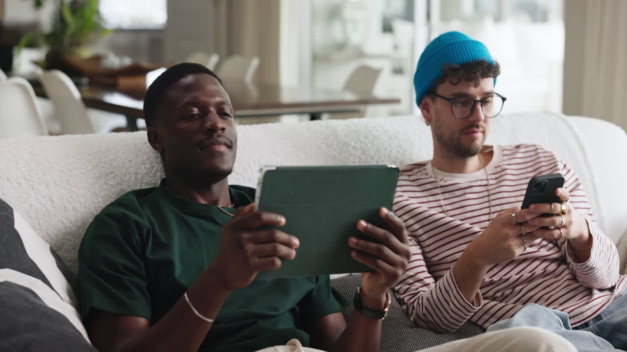 Due uomini che usano un tablet e uno smartphone su un divano
