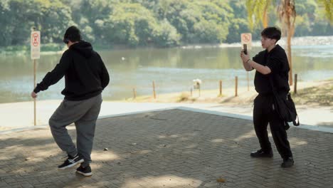 two young men filming dance content in a park by the river