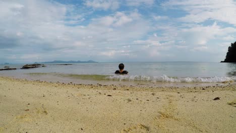 Caucasian-woman-sits-in-the-water-and-watches-horizon--low-angle-shot-from-behind