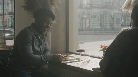 couple sitting and waiting order in cafe african american man and asian woman sitting at the table near window and waiting order in cafe with modern design waitress brings delicious dishes to multi ethnic guests concept of public eating