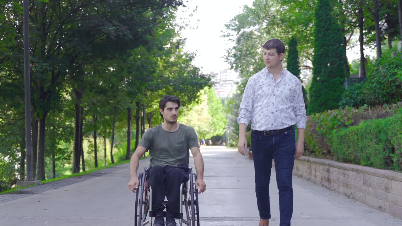 Disabled teenager is driving his wheelchair and talking to his friend walking next to him.