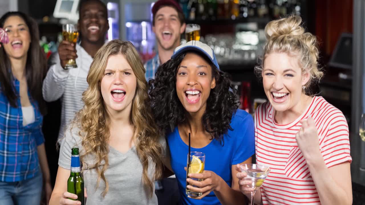 Felici tifosi sportivi, uomini e donne di diverse etnie, che guardano una partita al bar, facendo il tifo e bevendo.