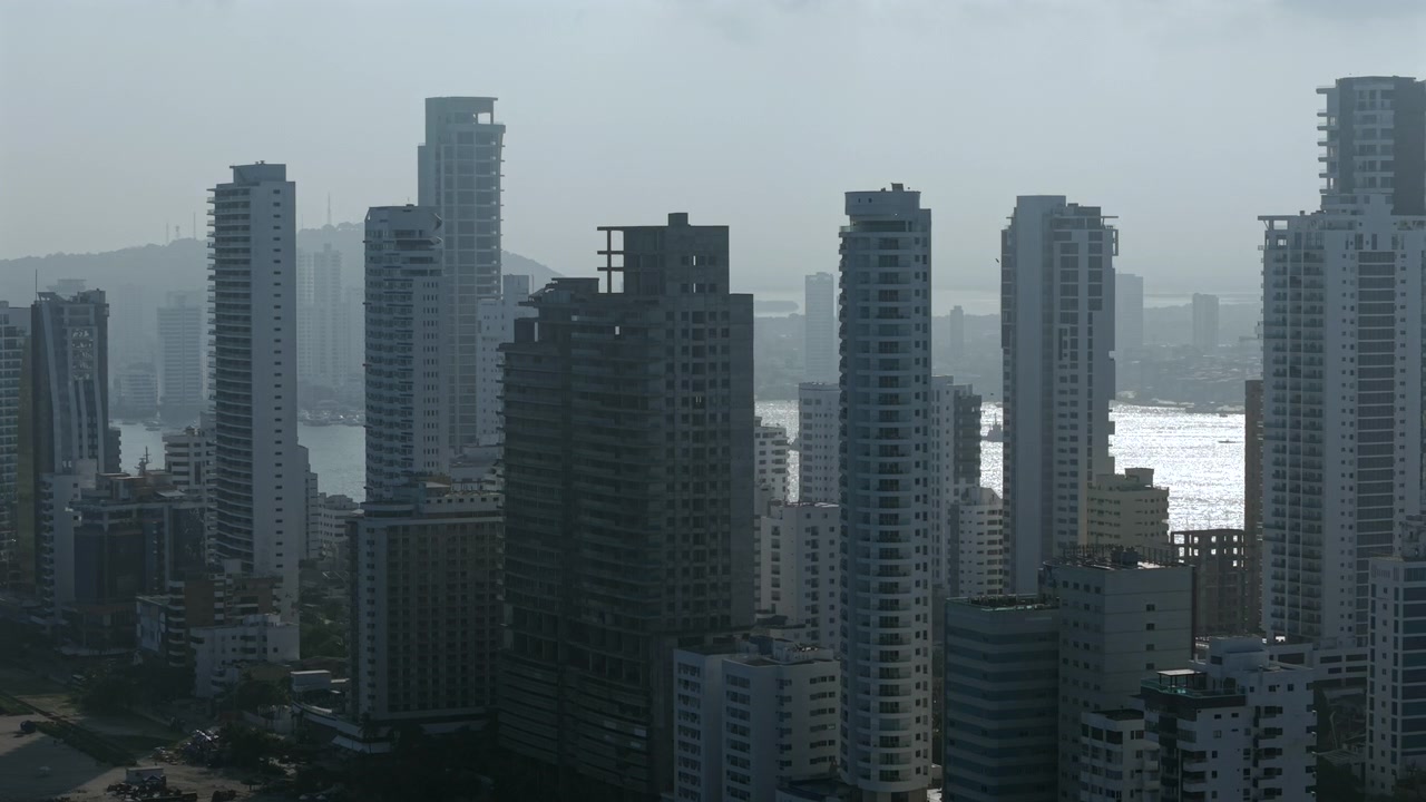 Imagens aéreas dramáticas exibem o horizonte de Bocagrande em Cartagena com imponentes edifícios modernos, água cintilante e uma névoa suave do crepúsculo. Grande angular, paisagem urbana, arquitetura urbana, atmosfera cinematográfica.