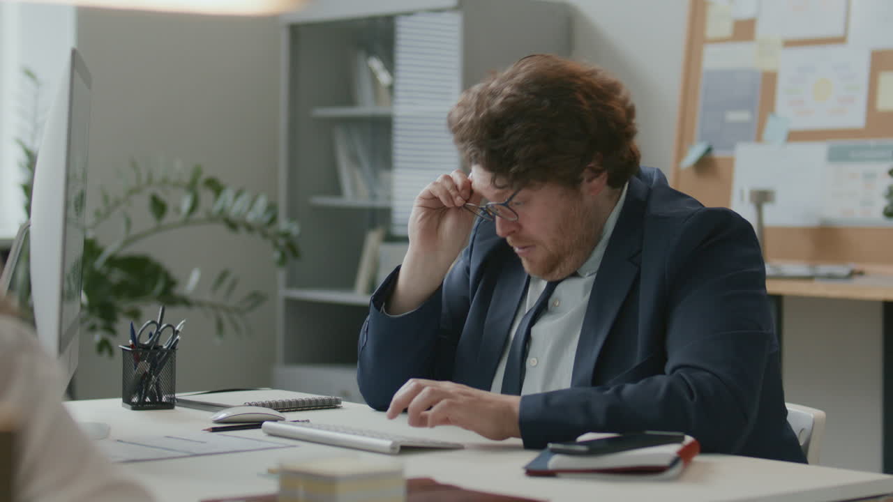 Uomo d'affari stanco che lavora al computer e si strofina gli occhi in ufficio