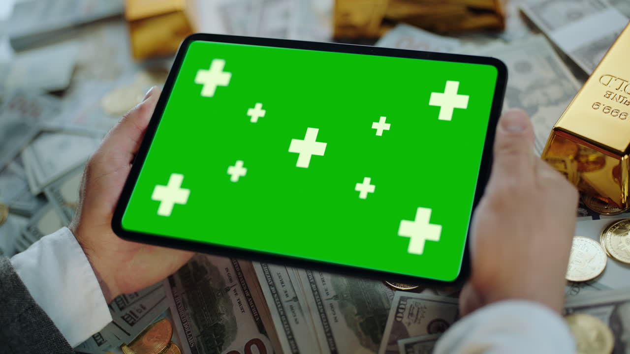 Tablet with Green Screen Surrounded by Money and Gold