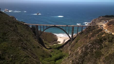 Una-Presentación-Cinematográfica-Del-Puente-Bixby-Creek,-Con-Imágenes-Aéreas-Y-De-Drones,-Que-Muestran-A-Los-Automovilistas-Conduciendo-Por-La-Carretera-Junto-A-Una-Impresionante-Vista-Del-Océano-Azul