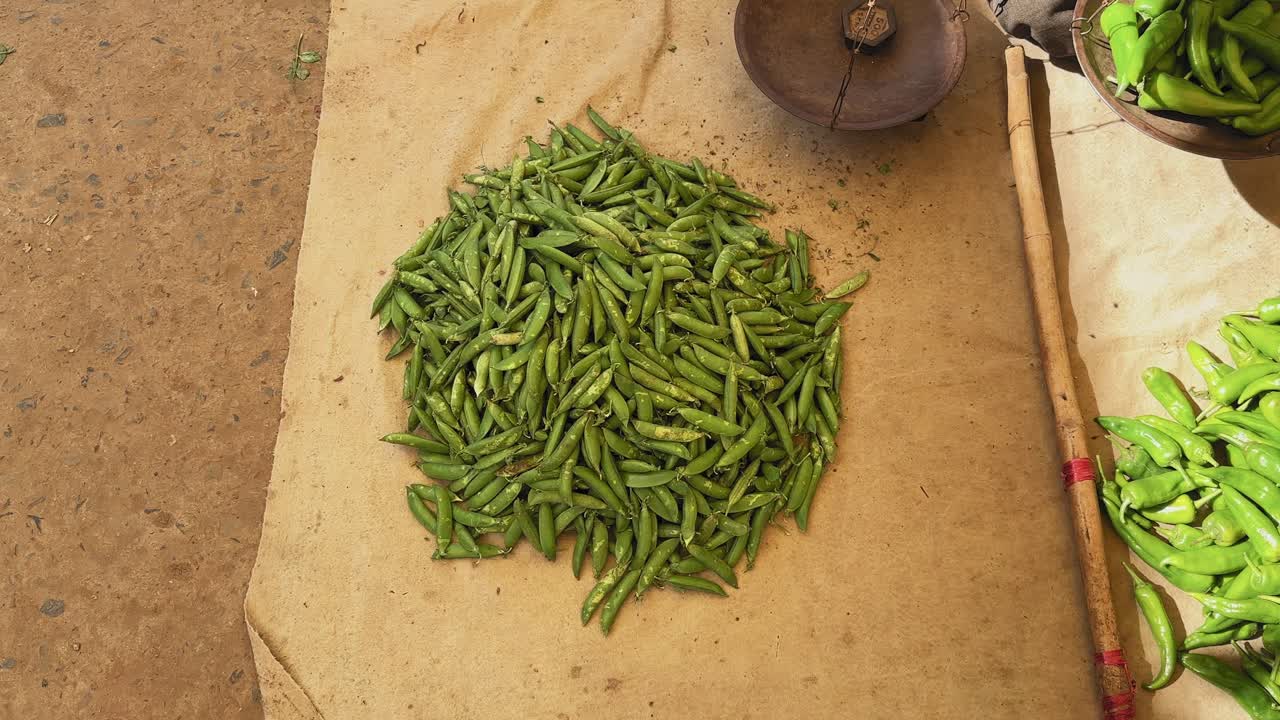 Circling shot of fresh green peas (matar) piled on a cloth in an Indian sabzi mandi, with warm light highlighting their vibrant color and natural market texture