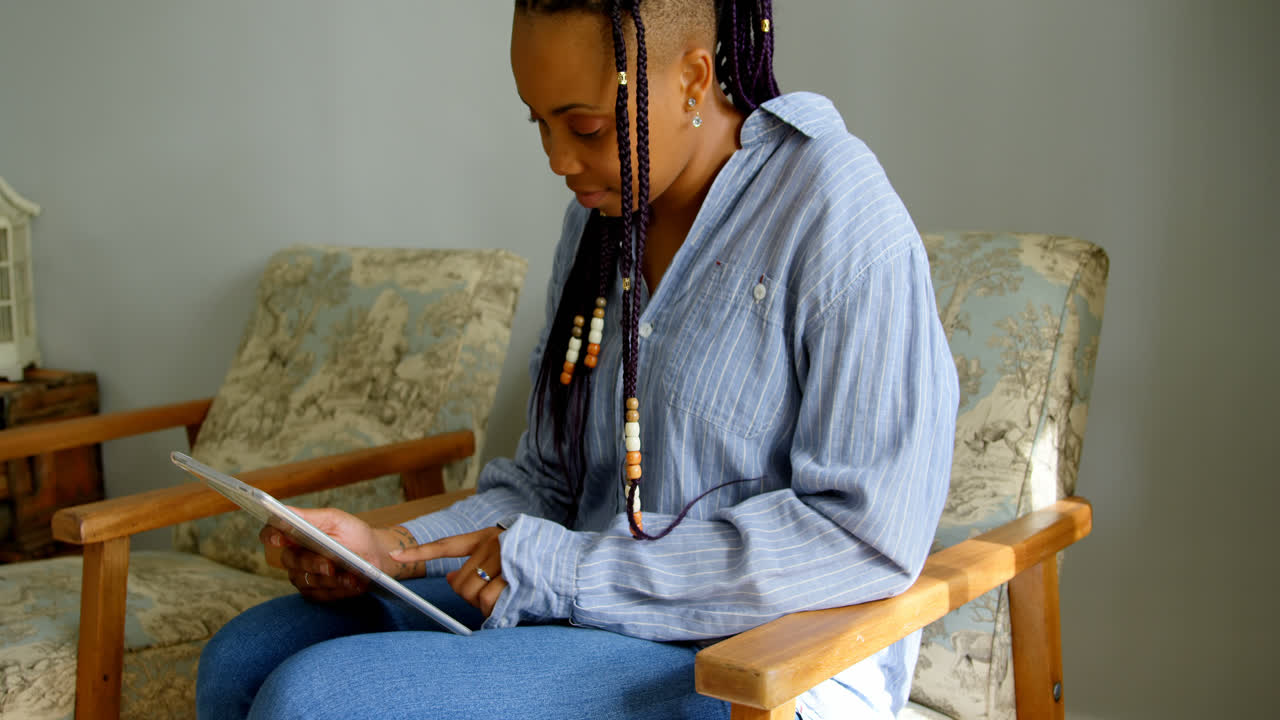 Side view of young black woman using digital tablet in living room of comfortable home 4k