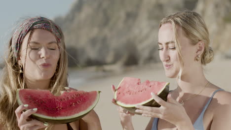 handheld shot of happy women eating watermelon on beach