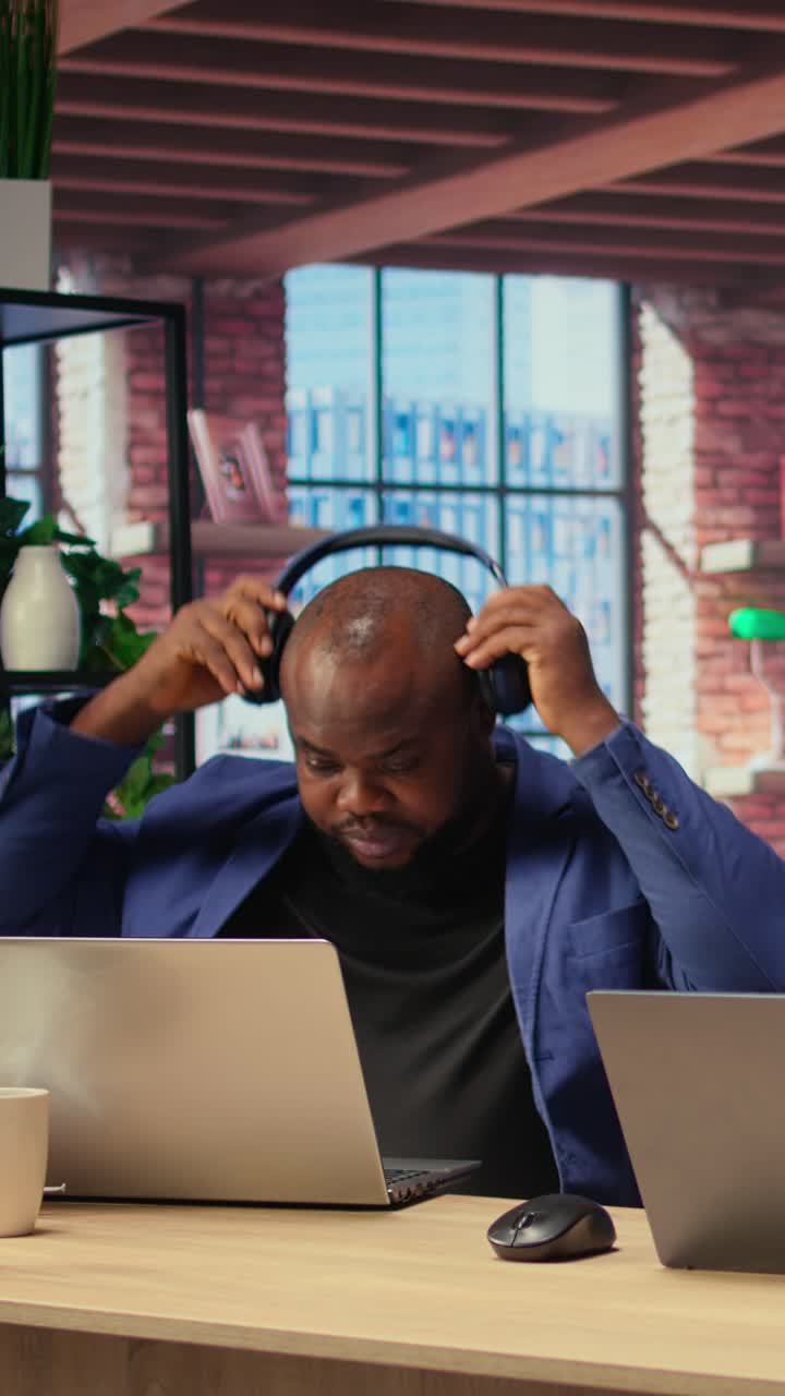 African American Man Working on Laptop and Putting on Headphones in Office