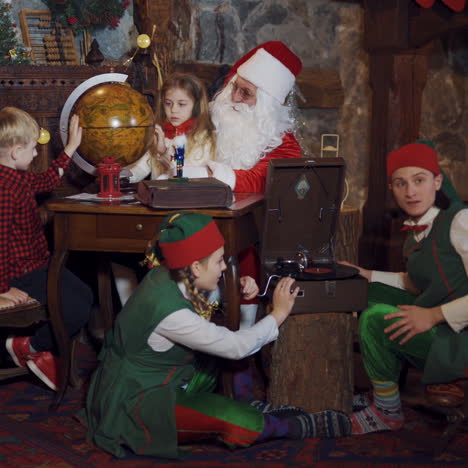 Santa Claus showing countries on the globe to little kids. Fairy elves trying to make music on old recorder in Santa's residence. Christmas time.