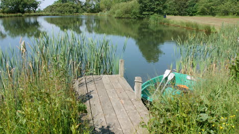 A-small-rowing-boat-and-wooden-dock-on-a-lake-pond-in-summer