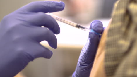 physician in blue surgical gloves giving senior female woman covid 19 vaccination at the medical center close-up