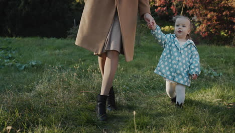 mom leads the hand of a little girl, walking in the park