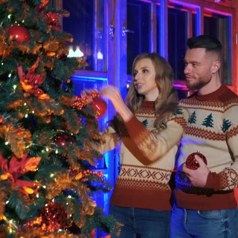 young couple decorates a christmas tree. happy guy and a beautiful girl getting ready for new year winter holidays celebration. festive mood in a modern cozy home.