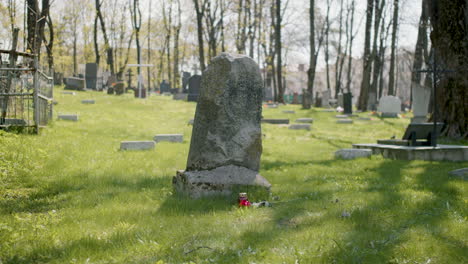 grabstein mit einer roten rose und einer grabkerze im gras auf einem friedhof an einem sonnigen tag 2