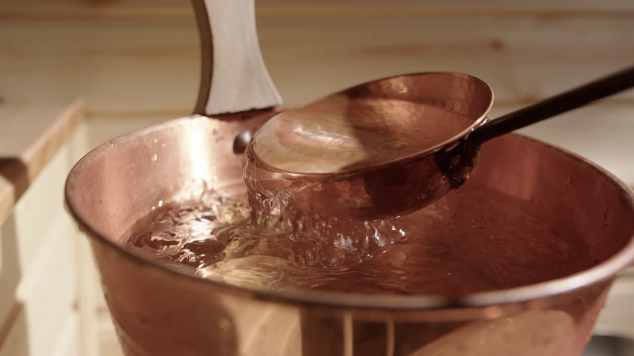 Fresh water scooped up with copper ladle from copper sauna bucket, slomo