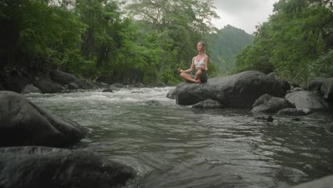 mujer en yoga sukhasana pose de loto en roca junto al río, búsqueda del alma