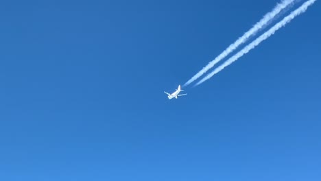 aerial view of a white jet flying at high altitude and its wake in a blue sky