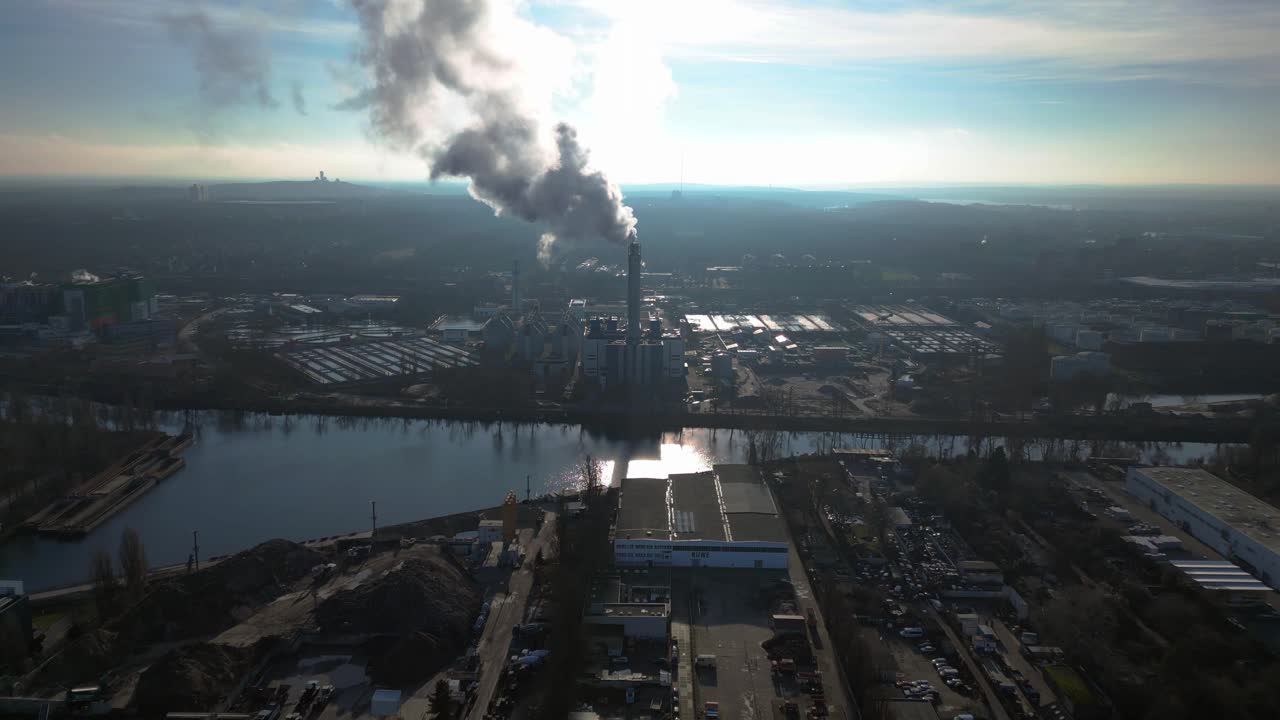 large industrial power plant emitting large amounts of smoke over the city Berlin next to a river on a sunny day. Magic aerial view flight fly push forward drone