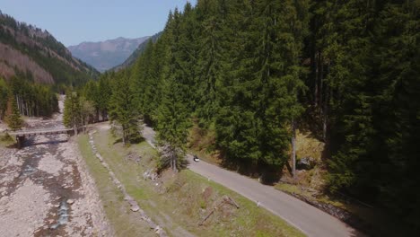 a winding road through a lush forest beside a rocky river in the mountains