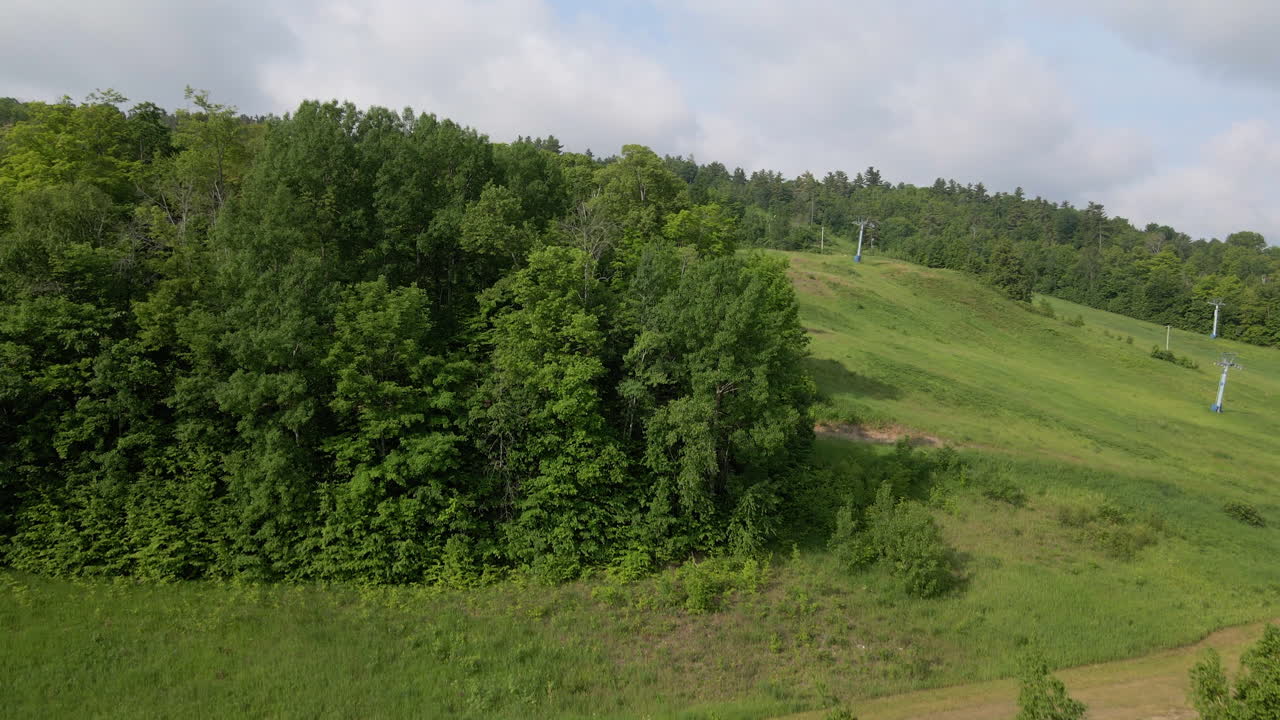 Aerial footage flying from lake up side of forest covered ski hill with chairlift on a clear summer day. Calabaogie Ontario