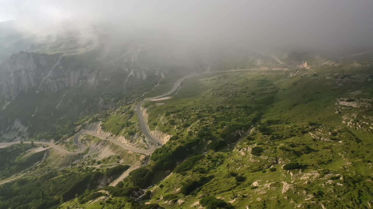White car driving down winding mountain road in Italy, forward aerial long shot