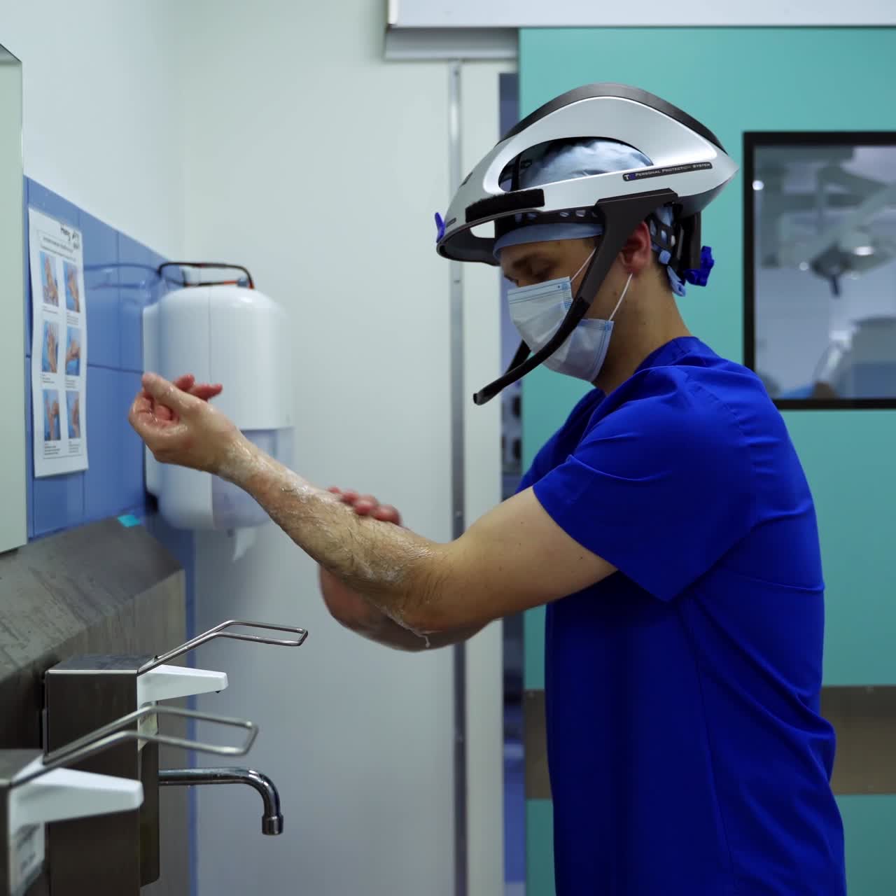 Doctor washes arms in clinic. Medical specialist in protective mask and hat washing his hands with a soap carefully. Hygiene in medicine.