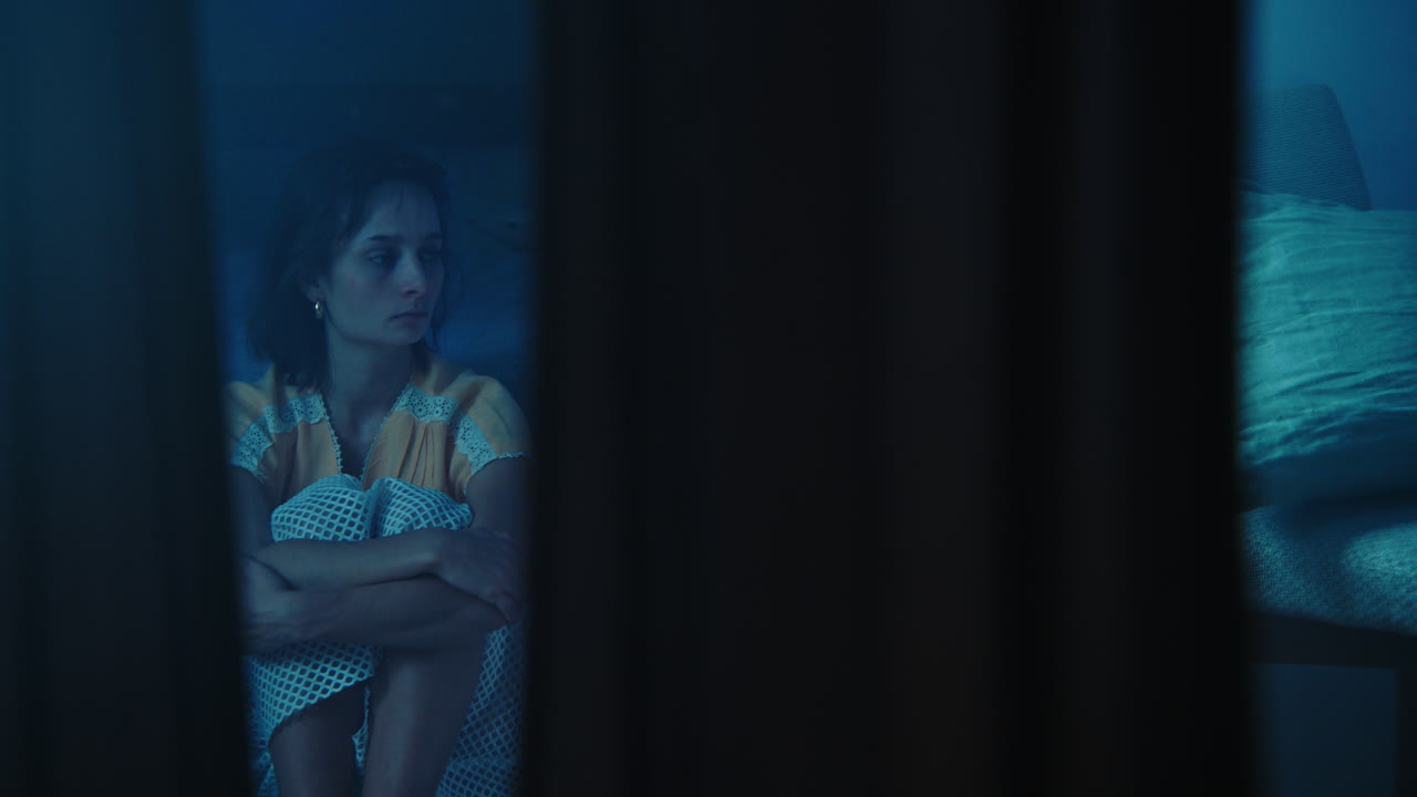 A traumatised and disoriented girl sits on the bedroom floor