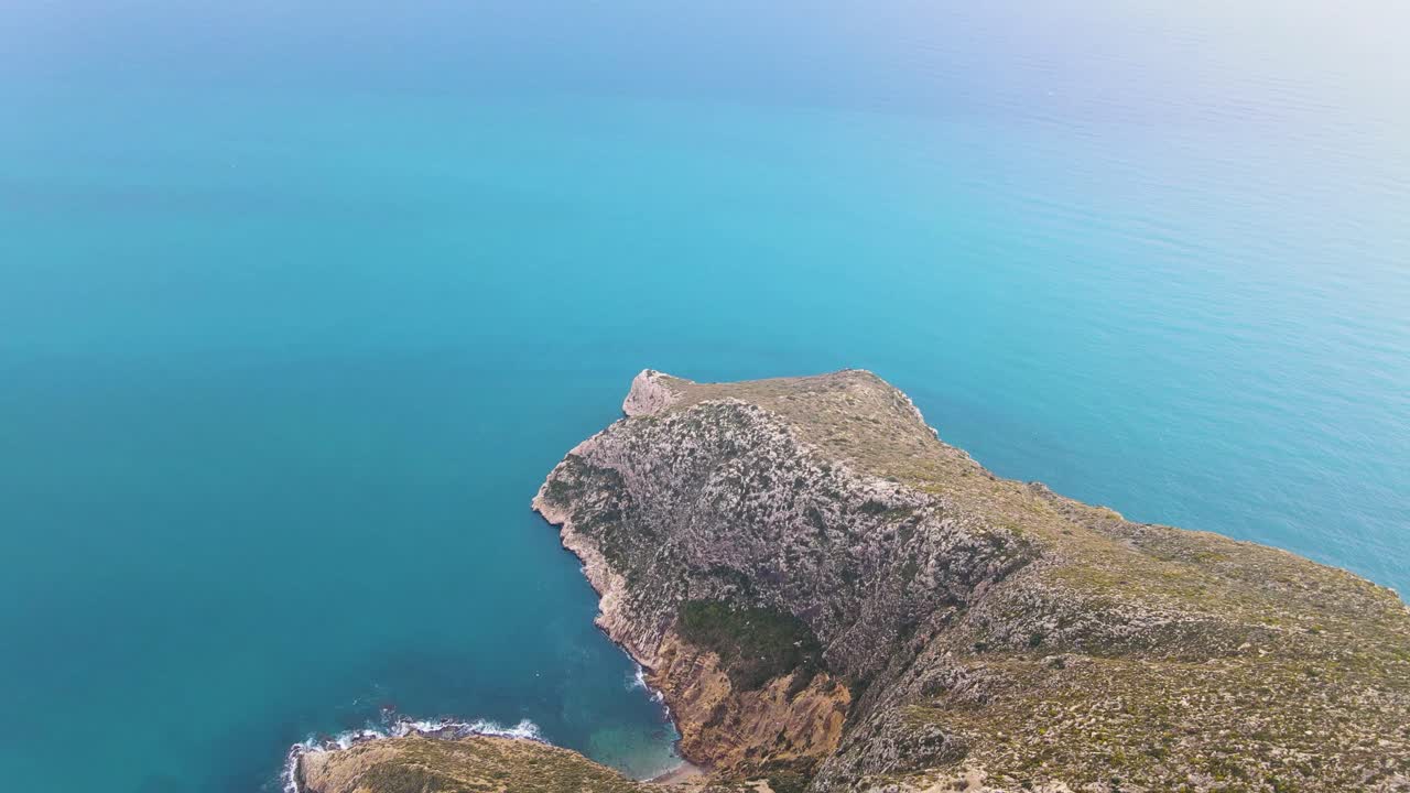 dolly aéreo de punta de toix en calpe, españa, mostrando la escarpada costa y las aguas turquesas bajo un cielo azul claro