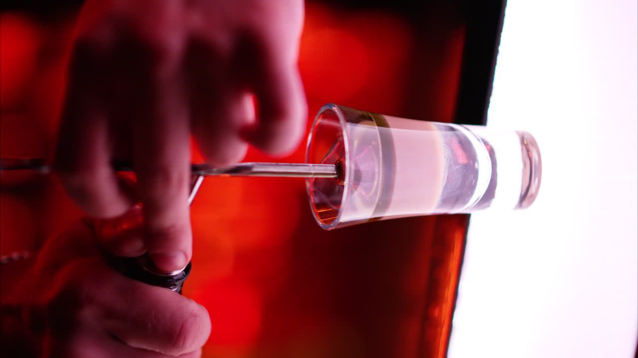 Barman making cocktail shots with liquor alcohol in three layers at the bar at night with red neon lights, slow motion vertical screen