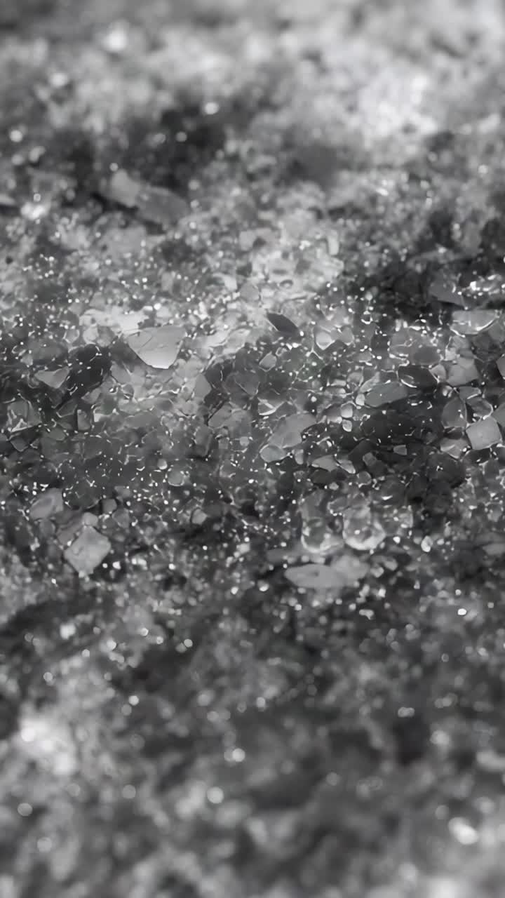 Vertical video: Cam panning and zooming showing wet ice drops macro on dark base, glints for detail