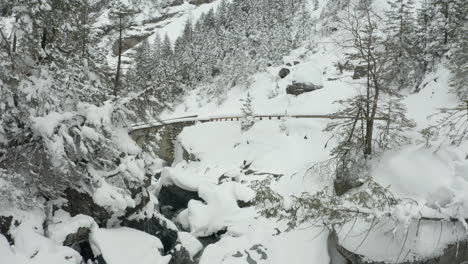 Moving-over-small-stream,-revealing-stone-bridge-in-snow-covered-landscape