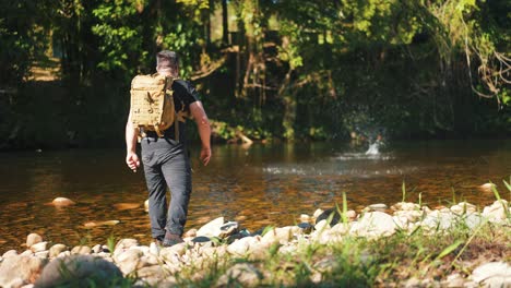 male hiker throwing a stone into the river making it bounce in slow motion in wild forest hot summer day, outdoor activity and travel concept