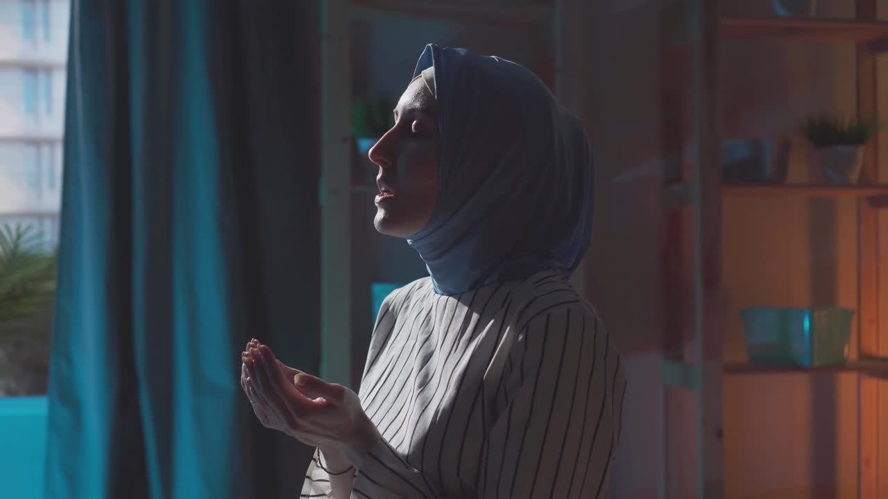 Primo piano di una bella giovane donna musulmana con l'hijab che prega in casa.