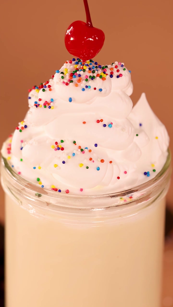 Primo piano al rallentatore di una ciliegia che cade su un milkshake alla vaniglia con panna montata e codette, illuminazione calda