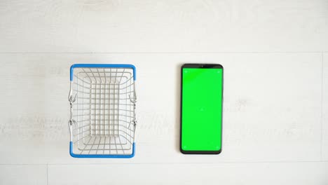 a phone with a green chromakey screen and a shopping cart on a white background. view from the top of the smartphone