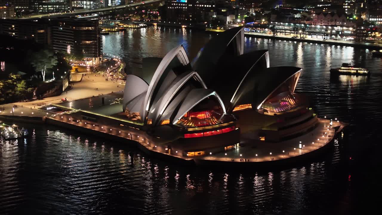 Amazing drone close up to Sydney Opera house during night. Illuminated buildings, cityscape.