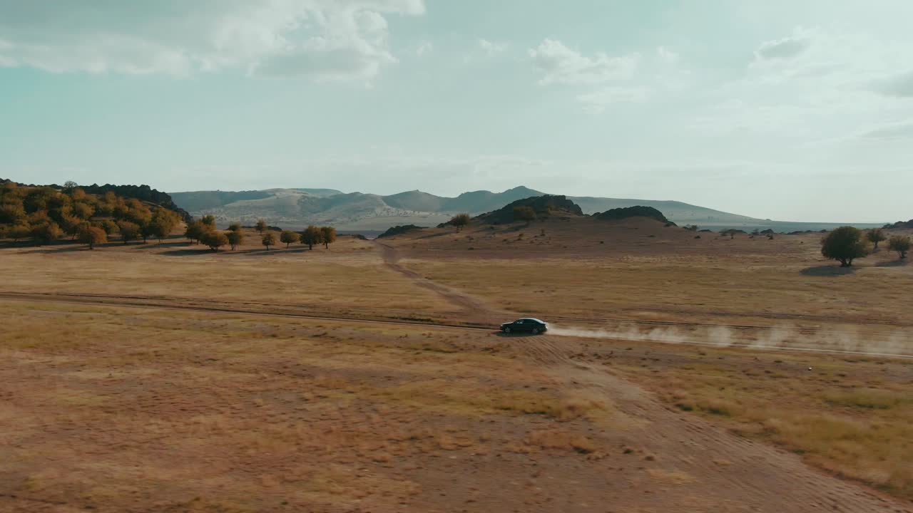 해가 지는 시점 에 시골 도로 에서 운전 하는 검은 차 를 추적 하는 드론  ⁇ , 먼지 가 가득 한 도로, 여행, 영화적 수준