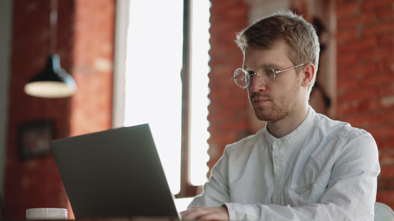 joven con gafas divertidas trabajando en su cuaderno con una taza de café fresco agradable y temprano en la mañana conseguir el negocio