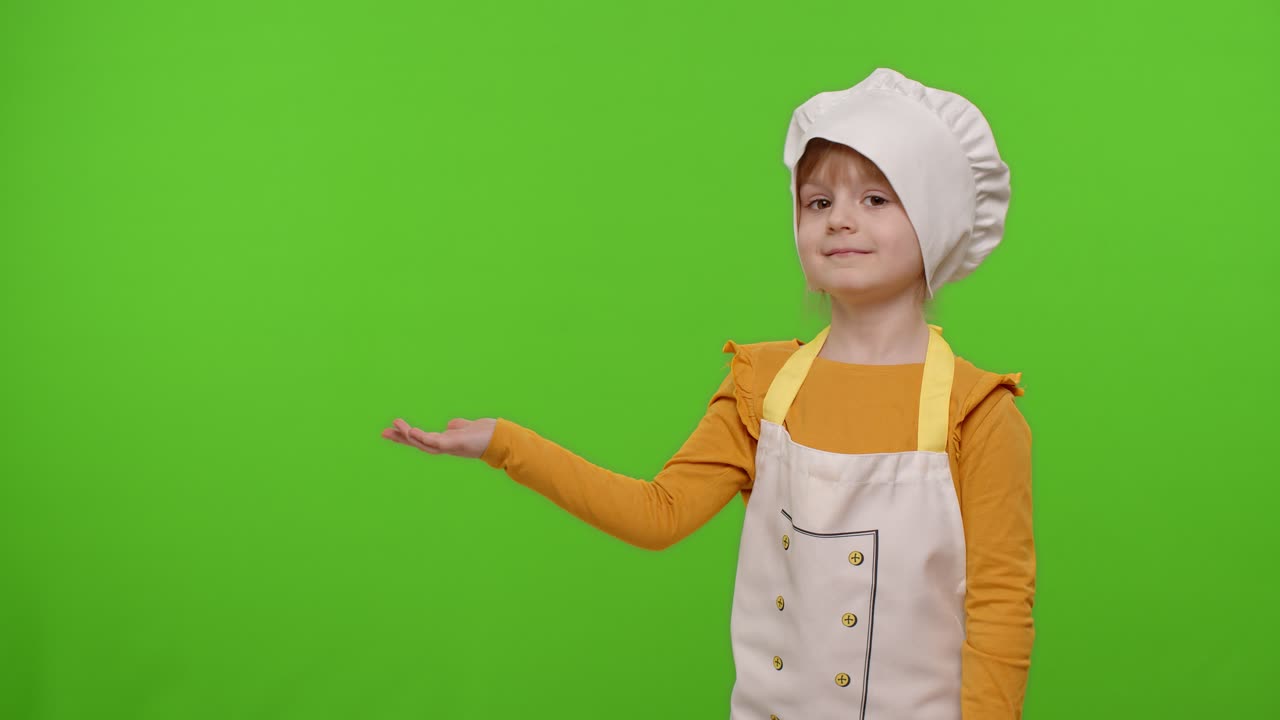Bambina vestita da chef che indica a sinistra su uno spazio vuoto, spazio per il tuo logo pubblicitario
