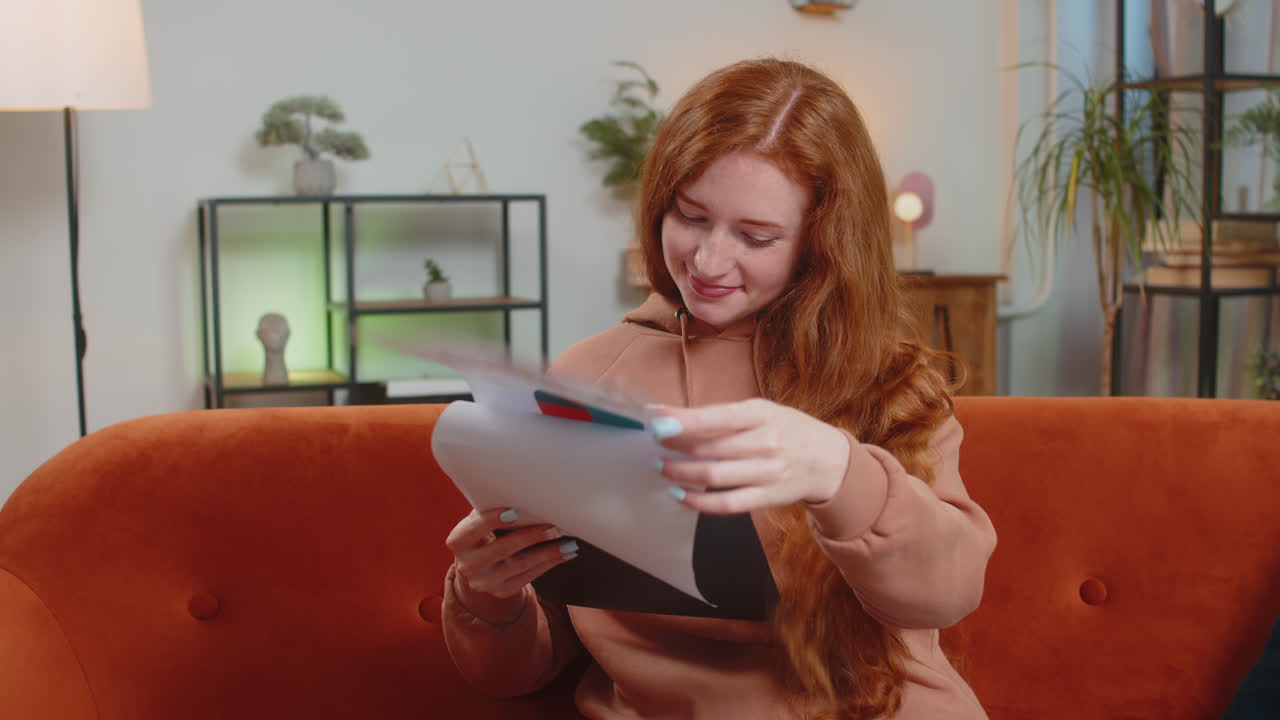 Woman accountant working with financial graph documents reading reports of income on sofa at home