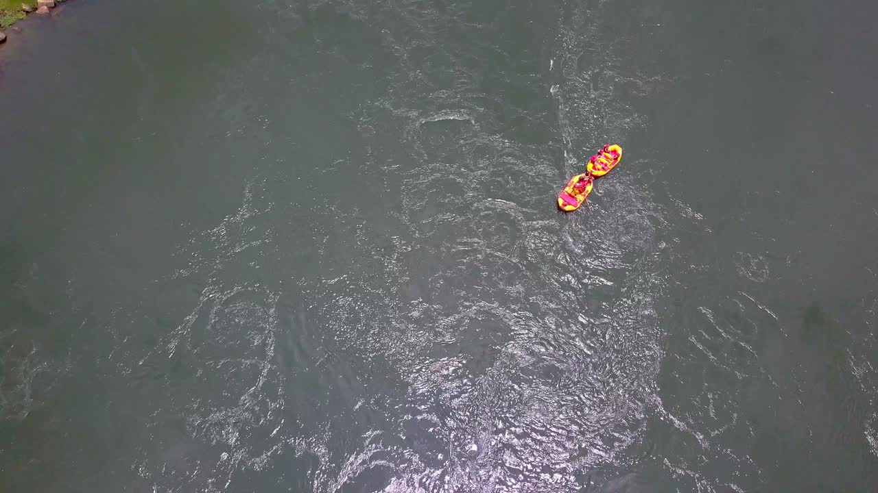 Top‑down aerial view of two inflatable rafts navigating the River Nile in Uganda, with rafters paddling downstream past green riverbanks and rocky edges