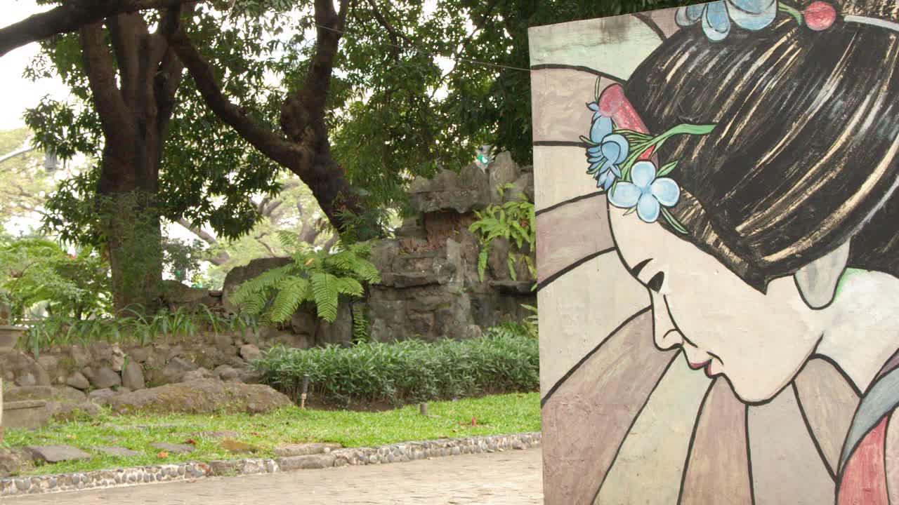 Una lenta carrellata rivela un murale colorato di geisha all'interno di un verde giardino tropicale.