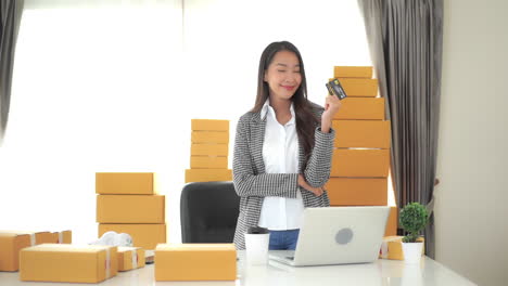 a young successful businesswoman surround by boxes waiting to be shipped hold up her credit card in triumph