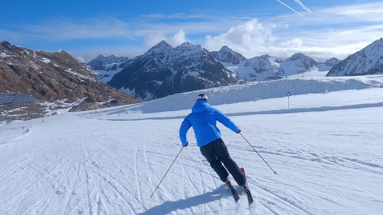 Sciatore alpino che scia ad alta velocità lungo le piste da sci con una vista alpina mozzafiato sul ghiacciaio e sulle grandi montagne. Piste da sci vuote e perfette e cielo blu in una giornata invernale soleggiata