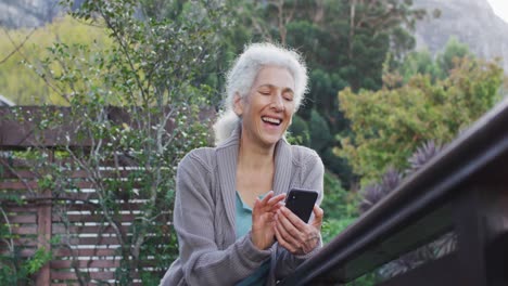 Portrait-of-senior-mixed-race-woman-using-smartphone-on-balcony