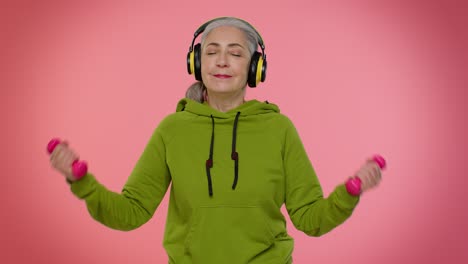senior granny woman listening music via headphones, working out, lifting pink dumbbells, healthcare