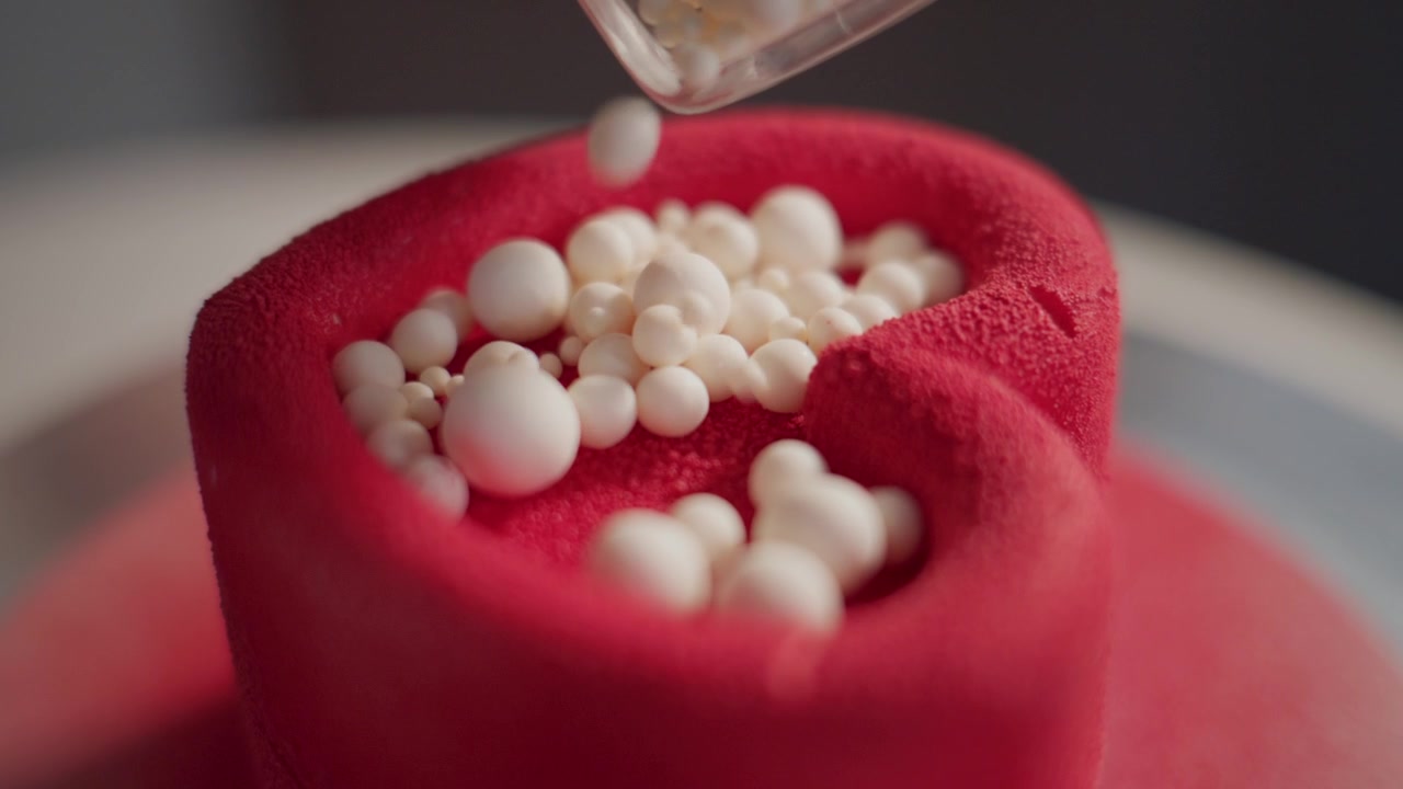 Torta rossa decorata con perle di zucchero bianche. Primo piano di glassa rossa liscia e vibrante. Piccole sfere cadono delicatamente sulla torta. Perfetto per blog di cibo o branding di dessert.